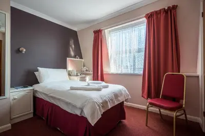a bedroom with a bed with red curtains and a red chair at Barrowfield Hotel in Newquay