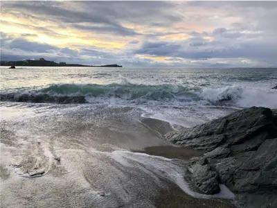 a beach with some waves and a rocky shore at Sunny Eco Home minutes from the beach (Tamsin) in Newquay