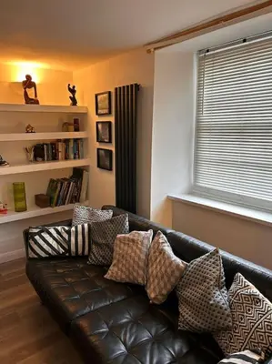 a living room with a black leather couch with pillows at Waves Cottage, Newquay. in Newquay