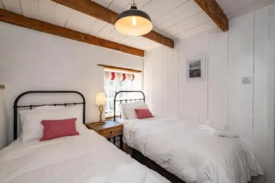two beds in a room with white walls and wooden beams at Sea Horses in Port Isaac