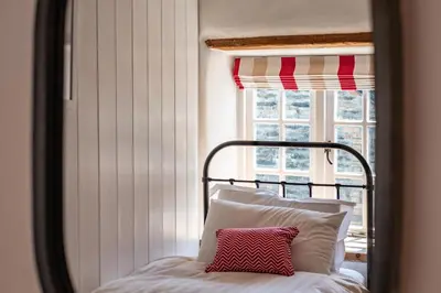 a bed with a red and white pillow in front of a window at Sea Horses in Port Isaac