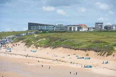 a group of people on a beach with buildings in the background at Bathsheba, Ocean 1 in Newquay