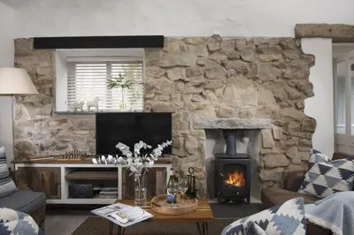 a living room with a stone wall with a fireplace at Rosehendra in Saint Erth