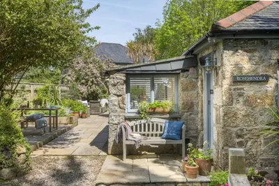 a stone house with a bench in a garden at Rosehendra in Saint Erth