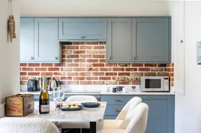a kitchen with blue cabinets and a brick wall at Beachspoke Loft in Redruth
