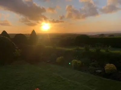 a sunset in a field with the sun setting at Beautiful family home, sea views, large garden in Port Isaac