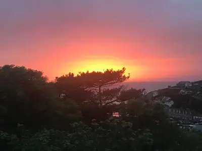 a sunset with a tree in the foreground at Cliffside 3 Bedroom House with Sea Views in Portreath