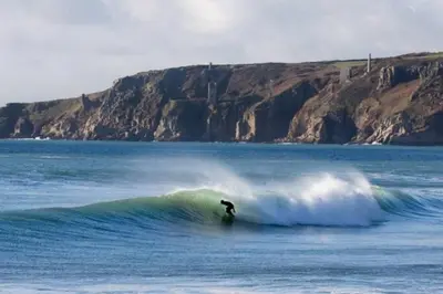 a person riding a wave on a surfboard in the ocean at Cliffside 3 Bedroom House with Sea Views in Portreath