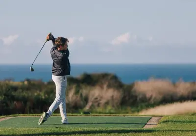 a woman swinging a golf club on a golf course at Cliffside 3 Bedroom House with Sea Views in Portreath
