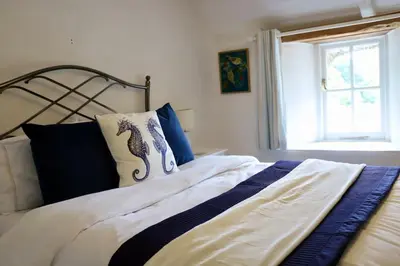 a bed with blue and white sheets and a window at Cosy thatched Cottage sleeps 6 near Portscatho! in Porthscatho