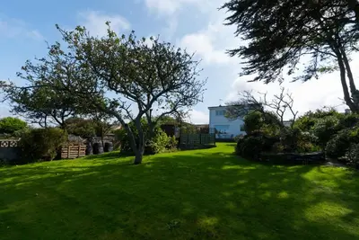 a green yard with a tree and a house at Talland Croft in Crantock
