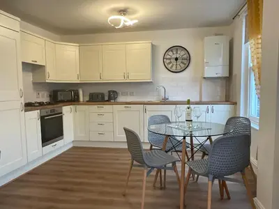 a kitchen with a table and chairs and a clock on the wall at Gregory Flats No. 1, by HomeInspire in Looe