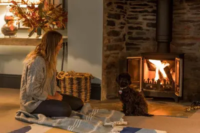 a woman sitting on the floor with a dog in front of a fireplace at Lostwithiel Stable House in Braddock