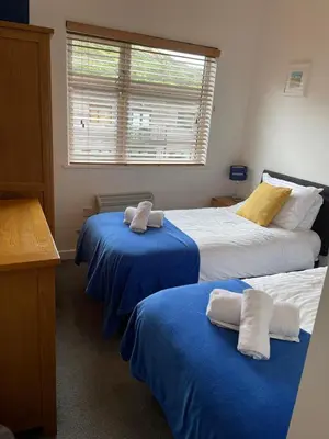 a bedroom with two beds with blue sheets and a window at Valentyne Beach House in Porthtowan