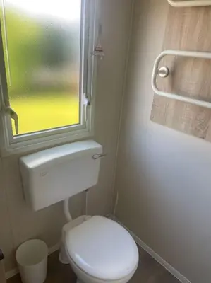a bathroom with a white toilet and a window at Delightful two bedroom caravan on Par Beach. in Par