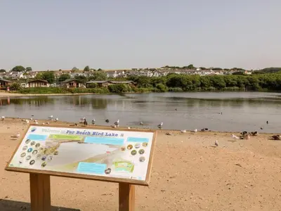 a sign on a beach with birds on the water at Delightful two bedroom caravan on Par Beach. in Par