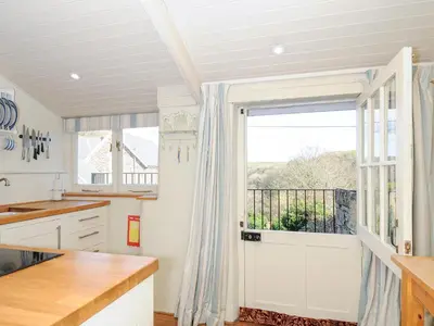 a kitchen with white cabinets and a large window at Lowen Cottage in Boscastle