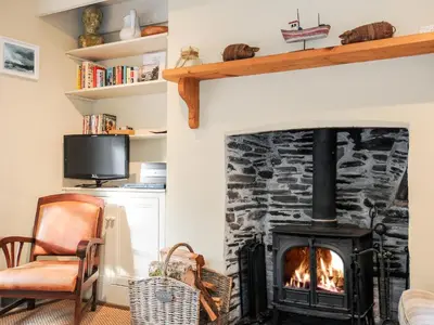 a living room with a fireplace and a chair at Lowen Cottage in Boscastle