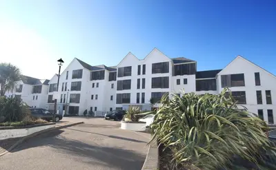 a large white building with palm trees in a parking lot at Surf's Up! in Newquay