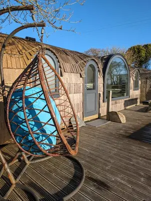 a wooden playground swing in front of a building at Jam First - Lydcott Glamping, Cornish Sea Views in East Looe