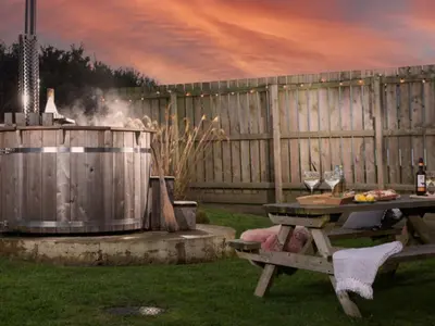 a picnic table and a grill with wine glasses at Chalet Hot Tub Lodge 2 by Interhome in Helston