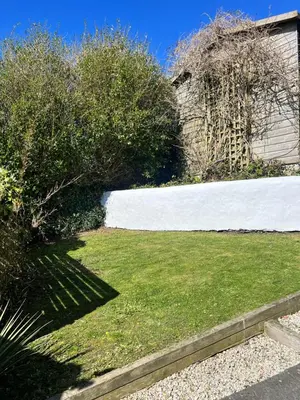 a yard with green grass and a white wall at Little Hillside in Porthtowan