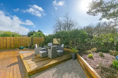 a garden with a wooden deck with chairs on it at Abelia in St Ives