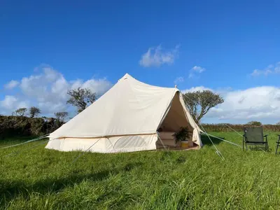 a white tent in a field with a chair at Trevena Cross Glamping & Camping in Helston