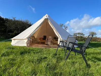 a white tent with two chairs in a field at Trevena Cross Glamping & Camping in Helston