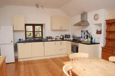 a kitchen with white cabinets and a wooden floor at Goodrevy Barn in Launceston