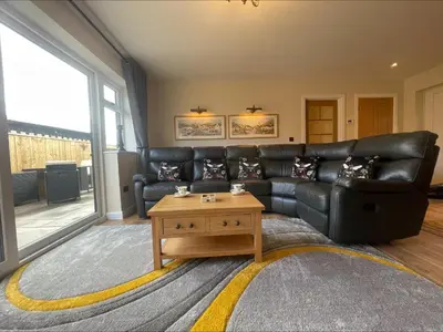 a living room with a black leather couch and a coffee table at Bumblebee Barn, Luxury contemporary holiday home in Perranporth