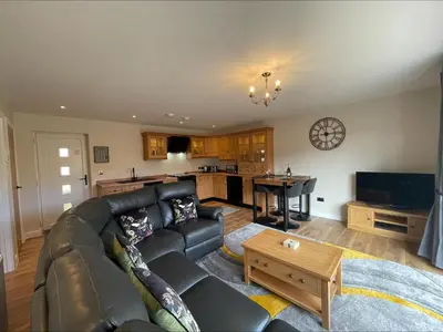 a living room with a leather couch and a kitchen at Bumblebee Barn, Luxury contemporary holiday home in Perranporth