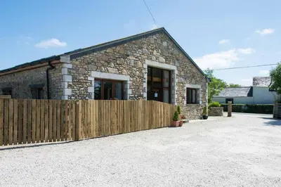 a stone house with a wooden fence in front of it at Trippet Cottage in Saint Breward