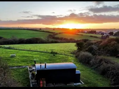 a building in a field with the sunset in the background at Shepherds haven hut Near Padstow in Saint Issey