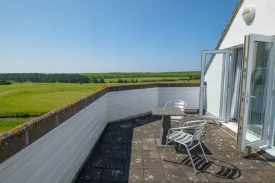 a patio with two chairs and a table on a balcony at Flat 1 Mawgan Porth Golf Club in Mawgan Porth
