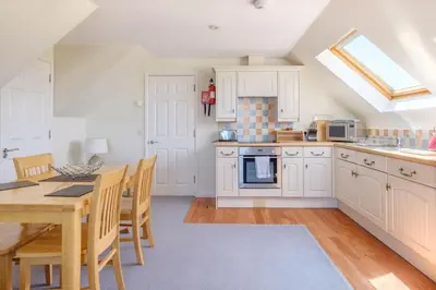 a kitchen with white cabinets and a table and chairs at Flat 1 Mawgan Porth Golf Club in Mawgan Porth