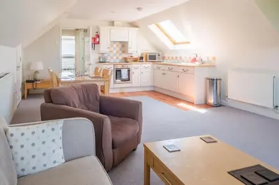 a living room with a couch and a kitchen at Flat 1 Mawgan Porth Golf Club in Mawgan Porth