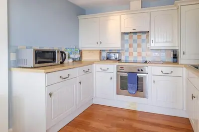 a white kitchen with white cabinets and a microwave at Flat 2 Mawgan Porth Golf Club in Mawgan Porth