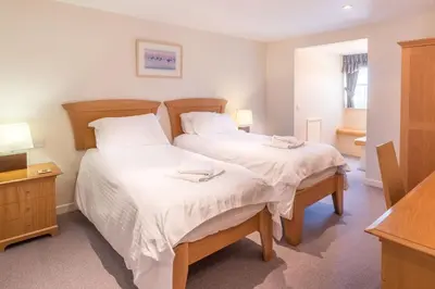 a bedroom with two beds with white sheets and two lamps at Flat 2 Mawgan Porth Golf Club in Mawgan Porth