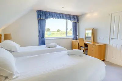 a bedroom with two beds and a desk and a window at Flat 3 Mawgan Porth Golf Club in Mawgan Porth