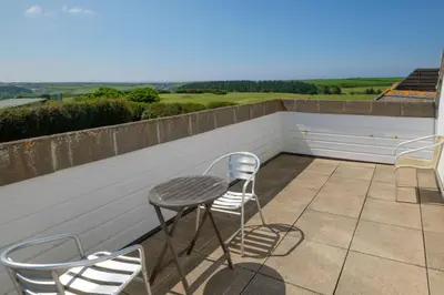 a patio with chairs and a table on a roof at Flat 3 Mawgan Porth Golf Club in Mawgan Porth