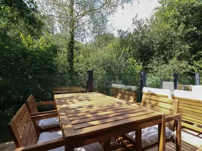 a wooden table and chairs on a patio with trees at 1 Streamside in Looe