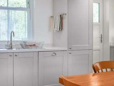 a kitchen with white cabinets and a wooden table at Bessborough in Saint Mawes