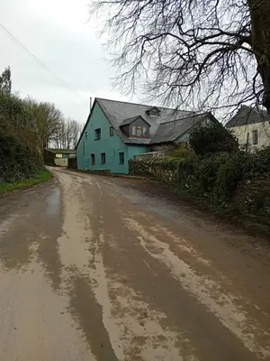 a dirt road with a blue house in the background at Robins Nest in Liskeard