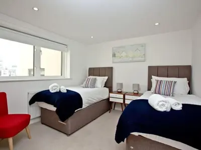a bedroom with two beds and a red chair at 15 Ocean Gate Newquay in Crantock