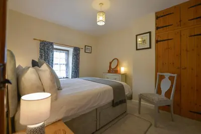 a bedroom with a bed and a chair and a window at Swallow Cottage in Helston
