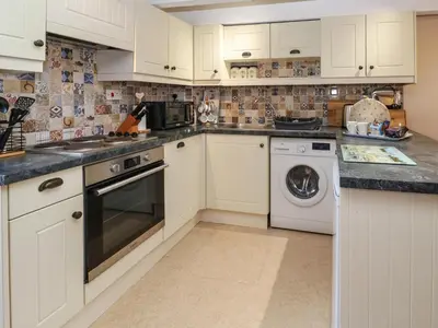 a kitchen with white cabinets and a washer and dryer at Swallow Cottage in Helston