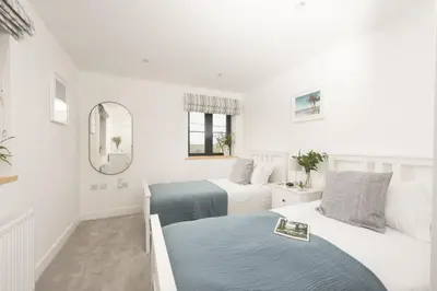 a white bedroom with two beds and a mirror at Atlantic Point, Porthleven - Free WiFi & Parking - Coffee Machine - Close to Harbour & Town in Porthleven