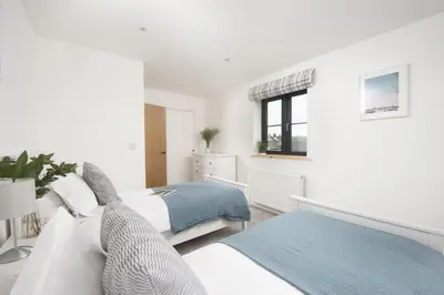 a white bedroom with two beds and a window at Atlantic Point, Porthleven - Free WiFi & Parking - Coffee Machine - Close to Harbour & Town in Porthleven