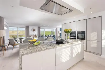 a kitchen with white cabinets and a living room at Sandyford, Holywell Bay - Sea Views - Walk to Beach - 2 Pets Allowed - Free Parking and WiFi in Holywell Bay